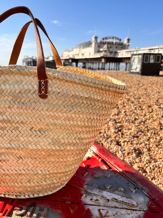 Woven straw bag with brown leather handles infront of the Brighton Palace Pier