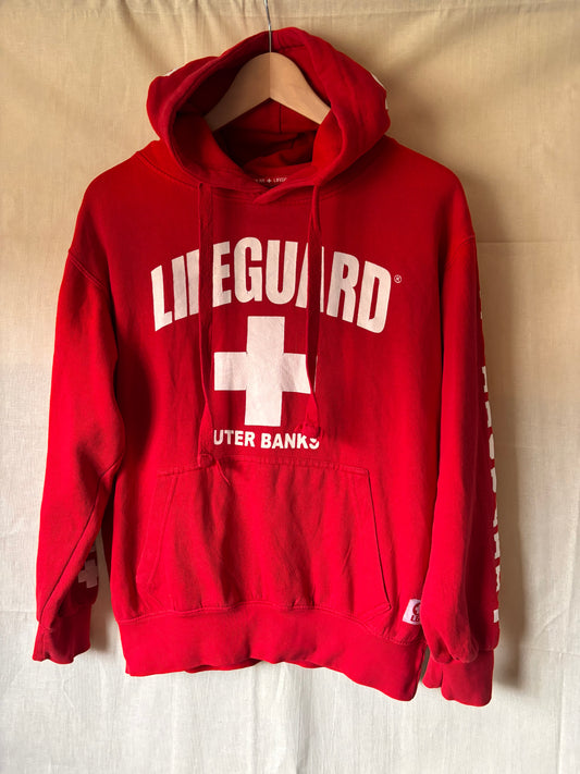 Red hoodie with 'Lifeguard' and a cross logo on a beige surface