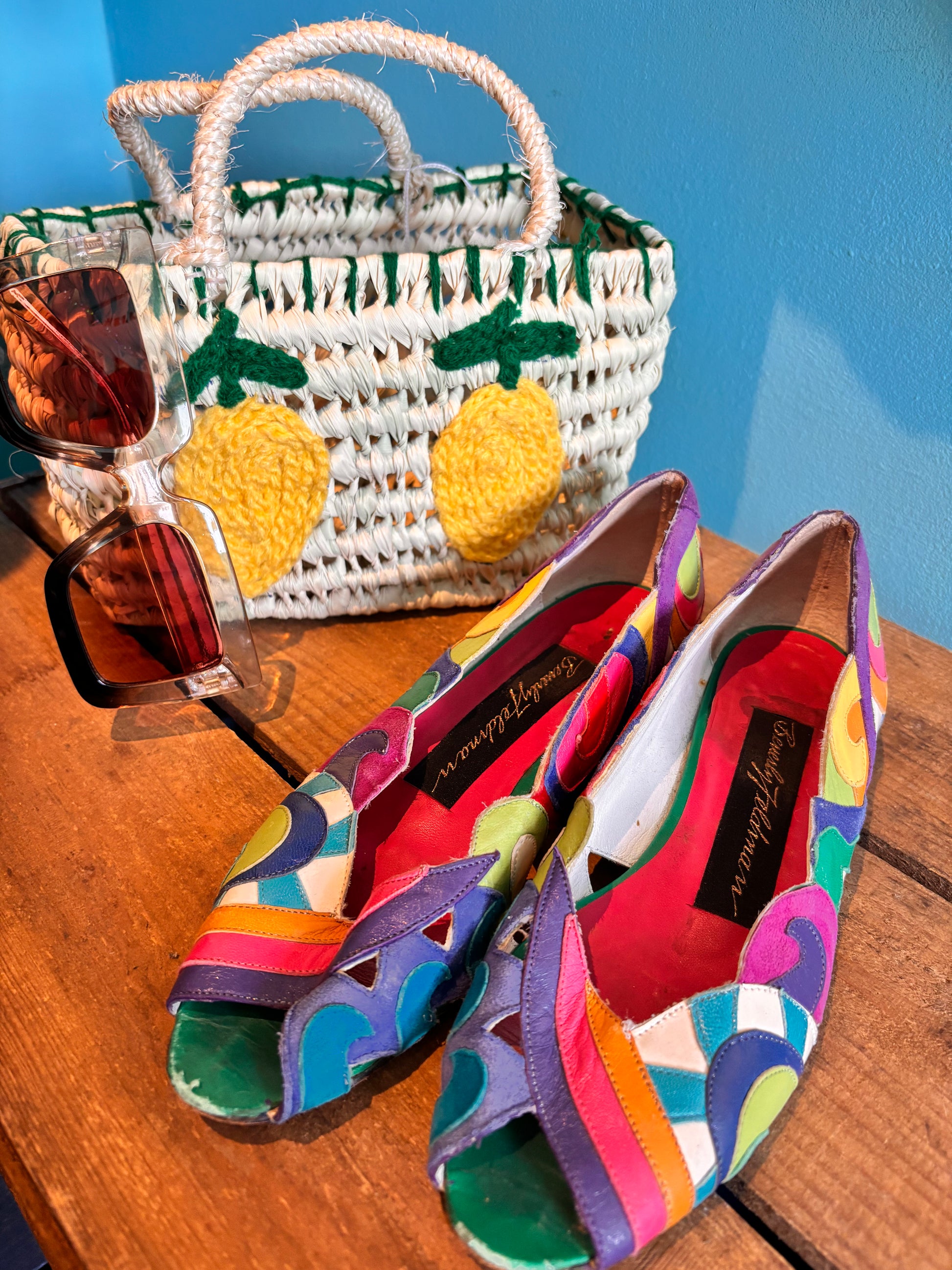 Colorful sandals with a woven bag and sunglasses on a wooden surface