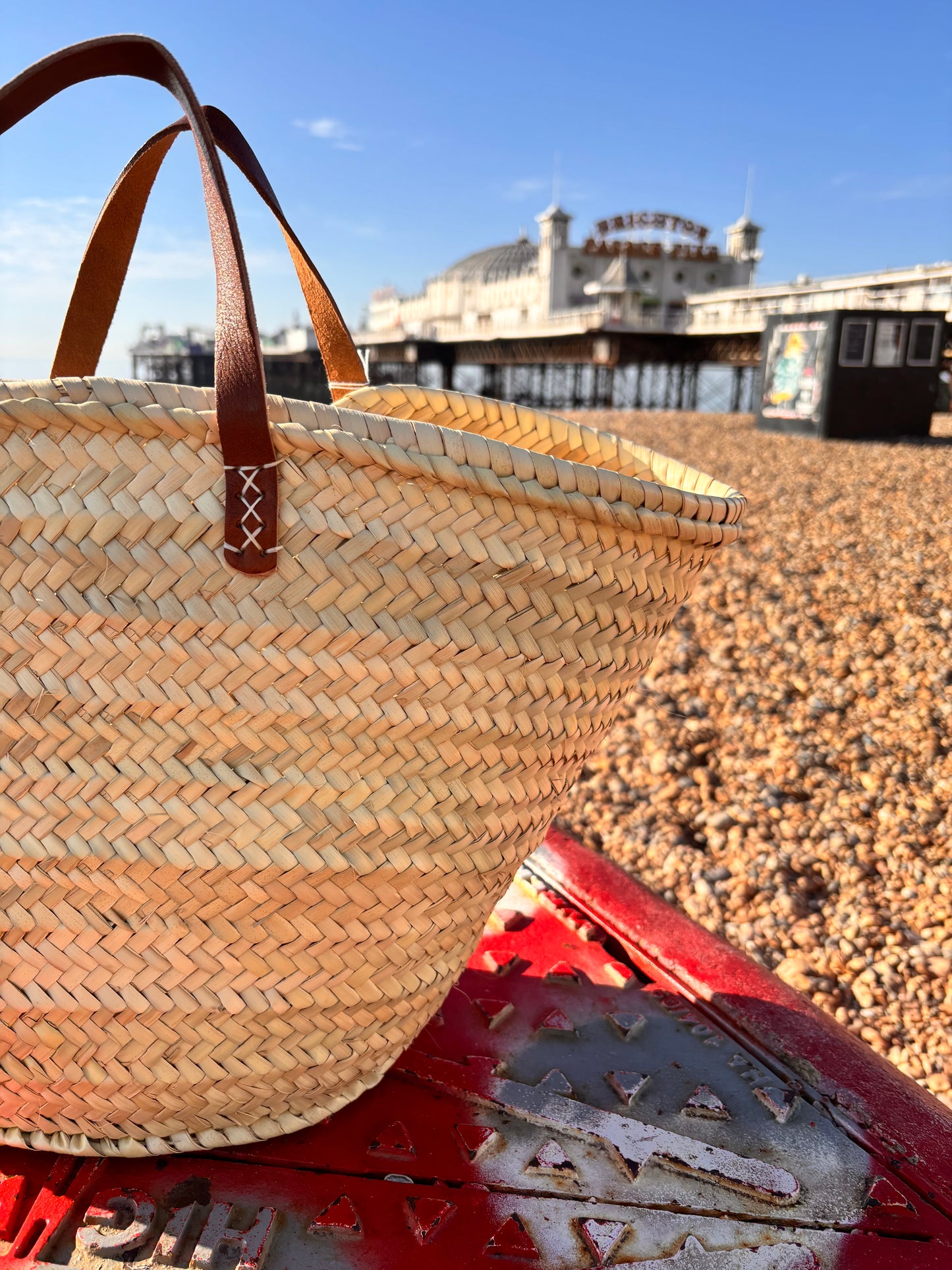 Woven straw bag with brown leather handles infront of the Brighton Palace Pier