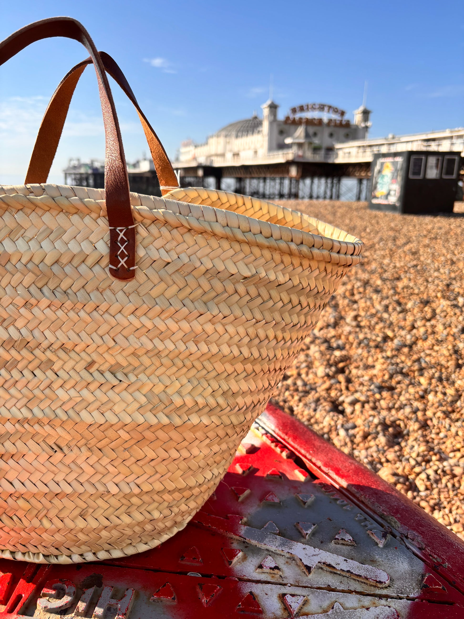 Woven straw bag with brown leather handles infront of the Brighton Palace Pier
