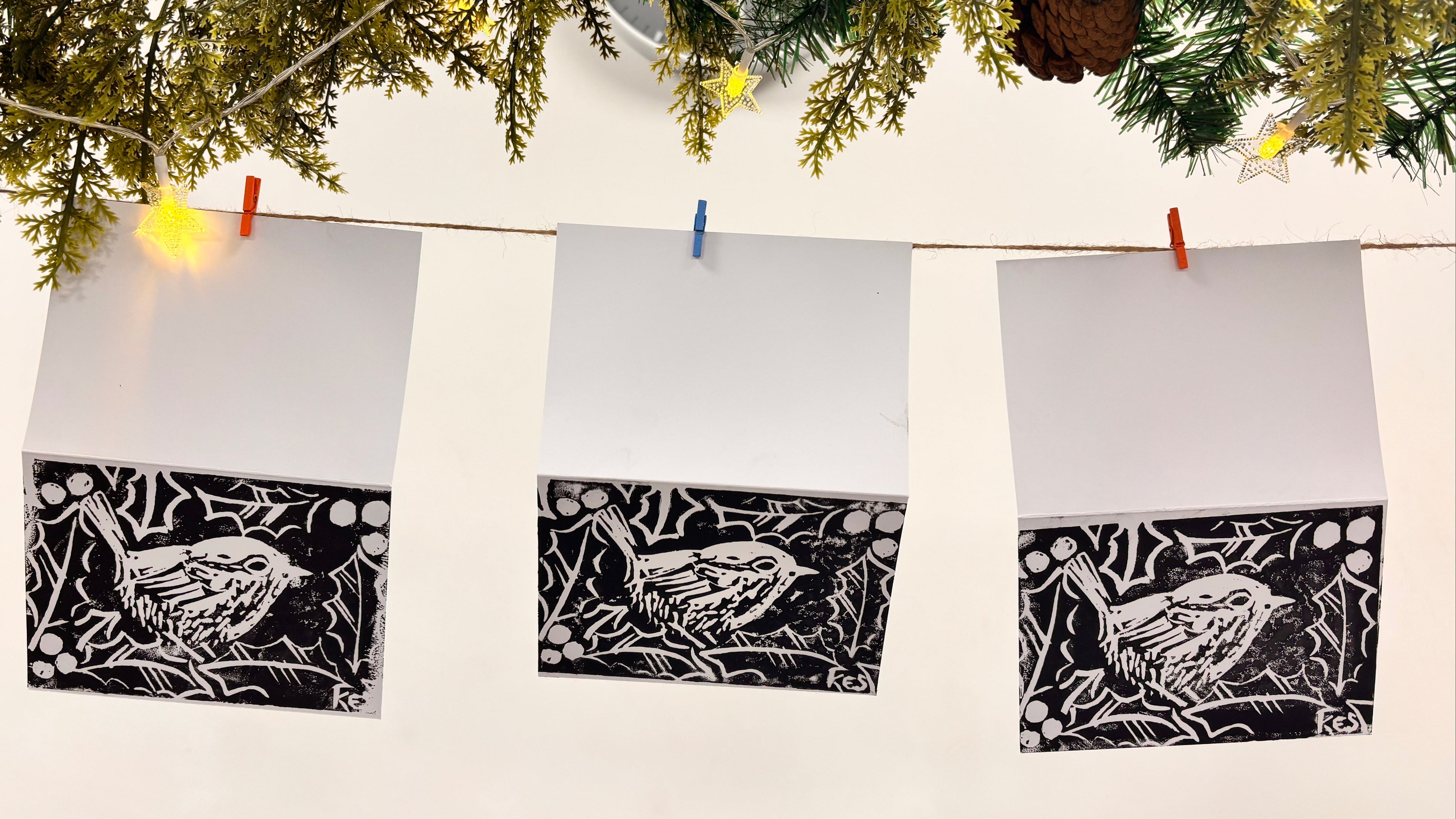Three lino prints of a bird design hanging on a line with greenery above.