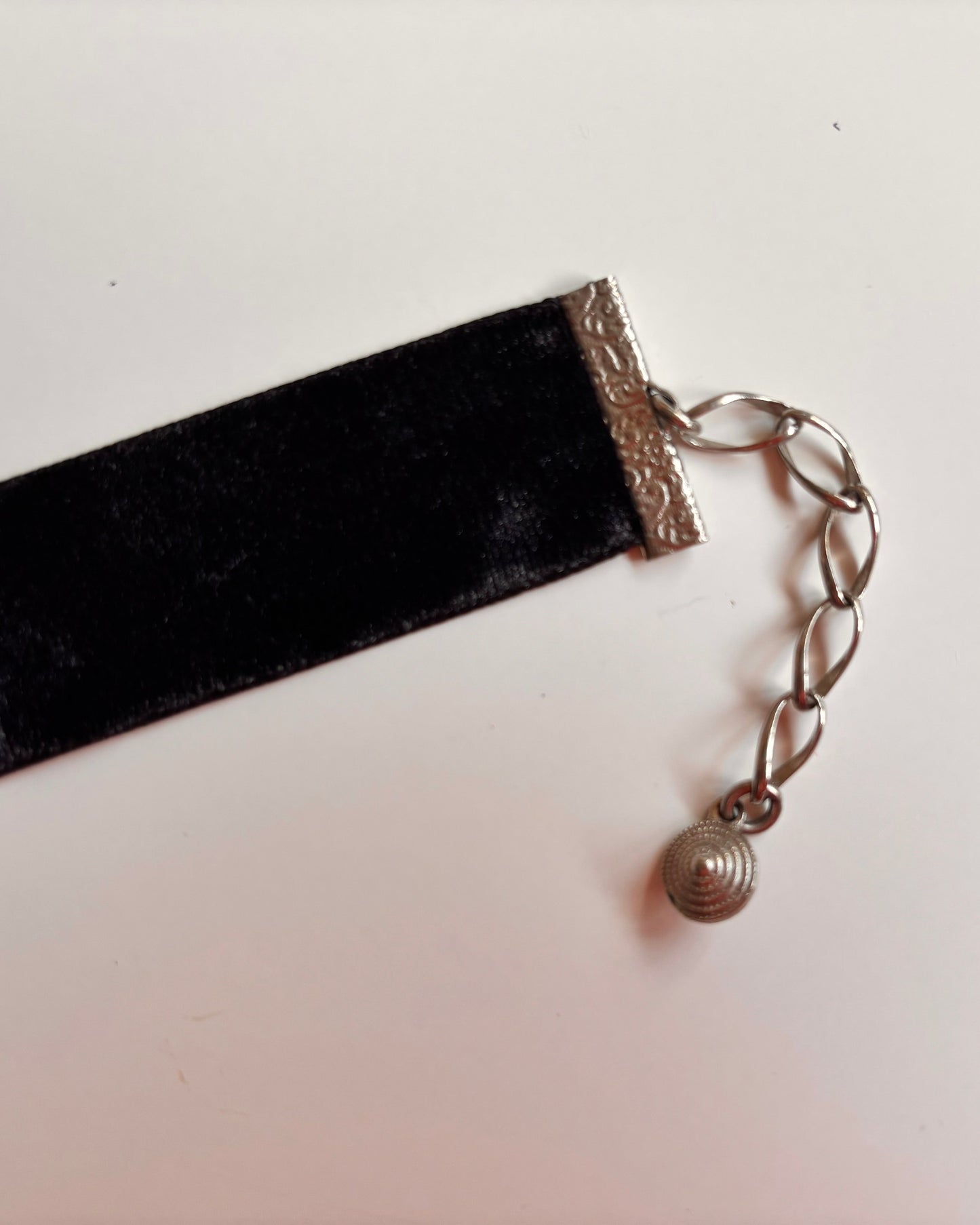 Black velvet ribbon choker with a silver chain and pendant on a white background