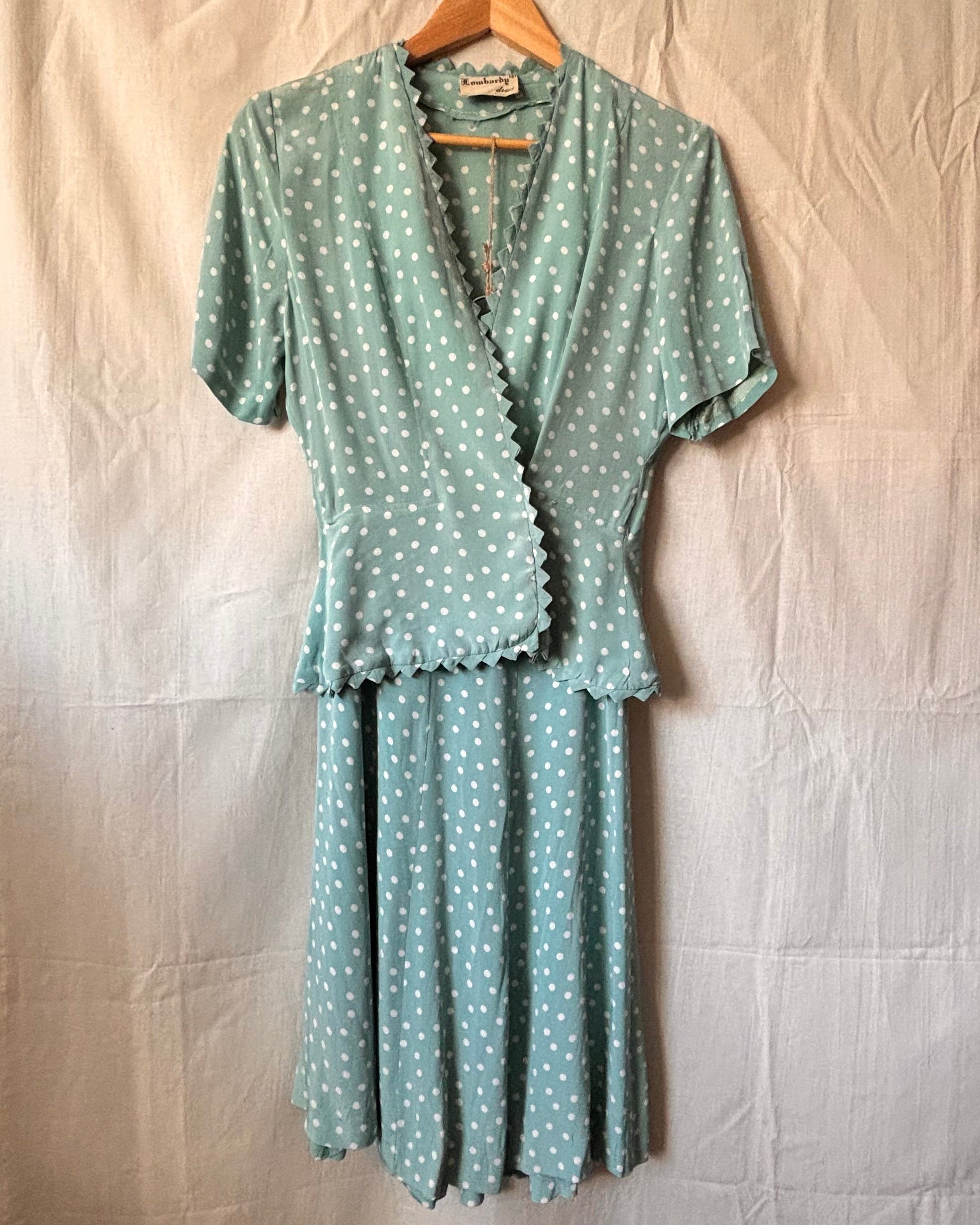 1940s powder blue polka dot two piece set. Features matching skirt and blouse on a hanger against a white backdrop