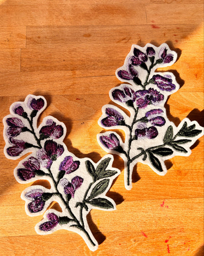 Two floral patches with purple flowers and green leaves on a wooden surface.