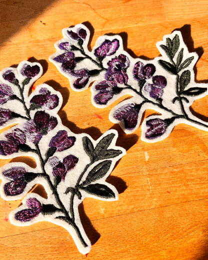 Two floral patches with purple flowers and green leaves on a wooden surface.