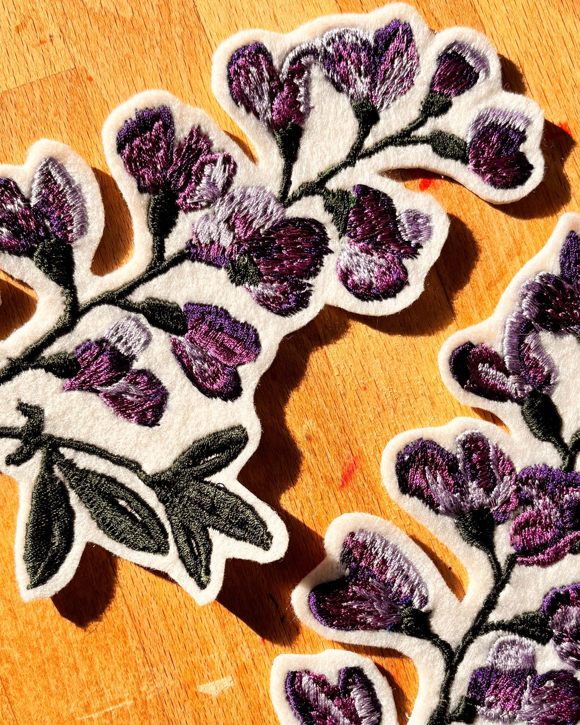 Two floral patches with purple flowers and green leaves on a wooden surface.