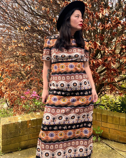Person wearing a patterned 1970s vintage boho dress standing outdoors with trees and grass in the background.