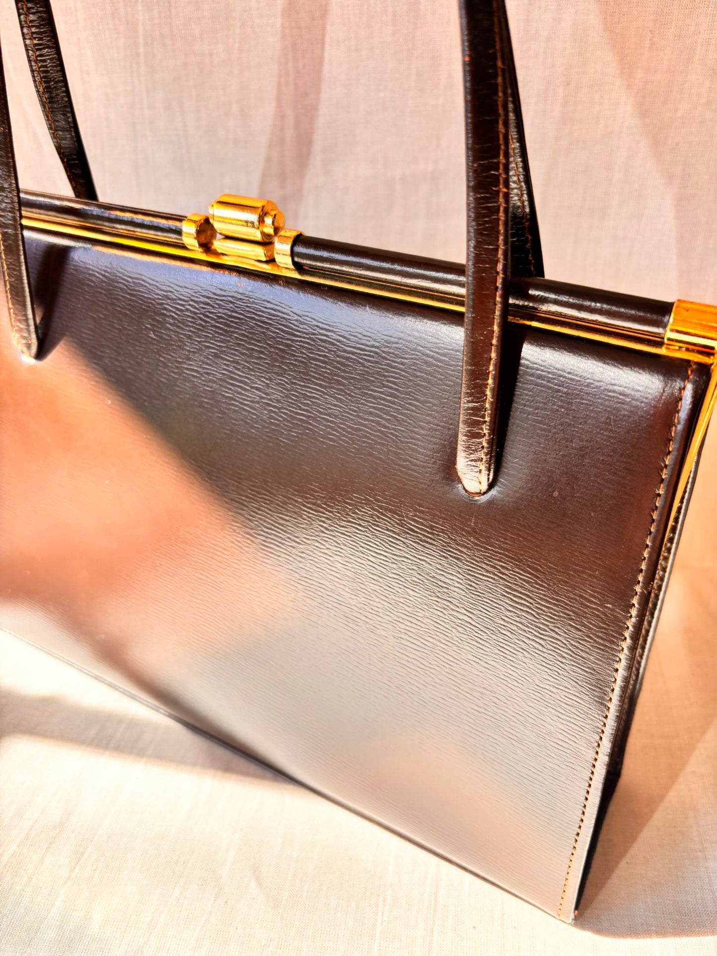Close-up of a brown vintage 1960s handbag with gold accents on a light background