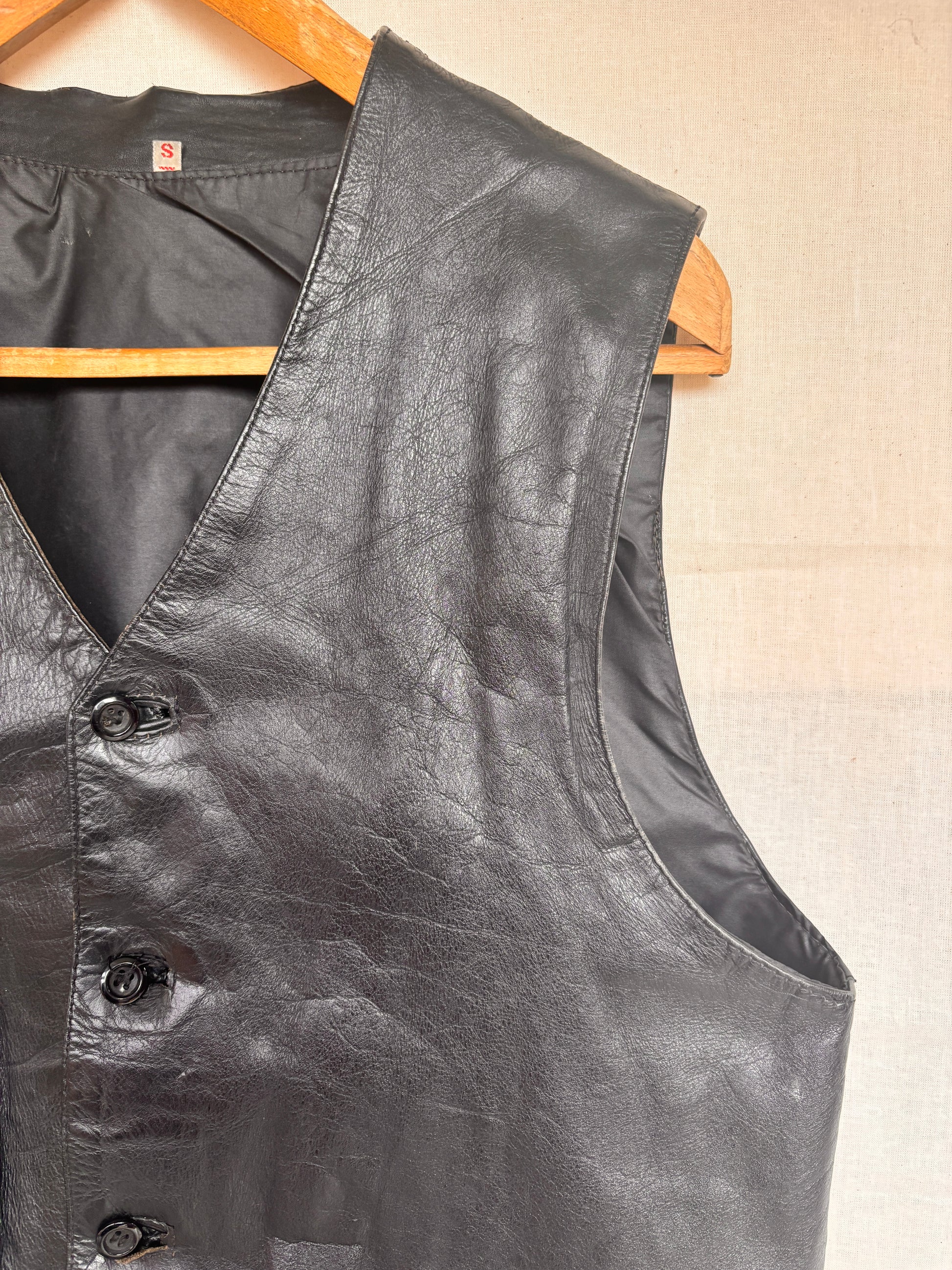 Black leather jacket on a wooden hanger against a beige wall.