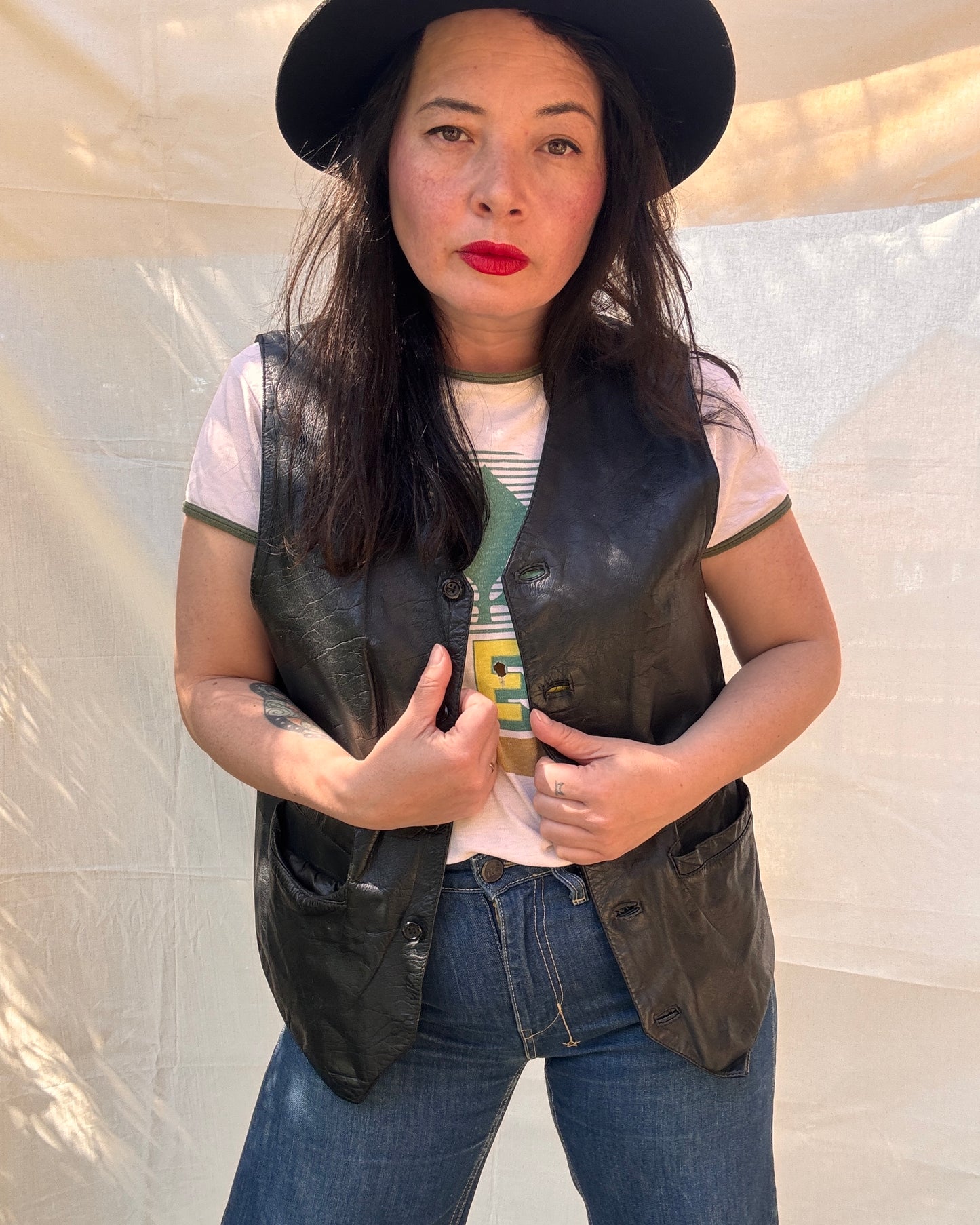 Woman wearing a black leather vest, white t-shirt, and blue jeans against a plain background